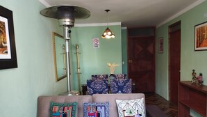A living room with a sofa, decorative pillows, a standing heater, a lamp, and a door. - Huaytusive (Puno)