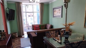 A living room with a sofa, a glass coffee table, a television mounted on the wall, and a window with curtains. - Huaytusive (Puno)