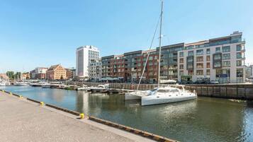 Eine Marina mit vertäuten Booten, eine Uferpromenade und moderne Gebäude im Hintergrund.