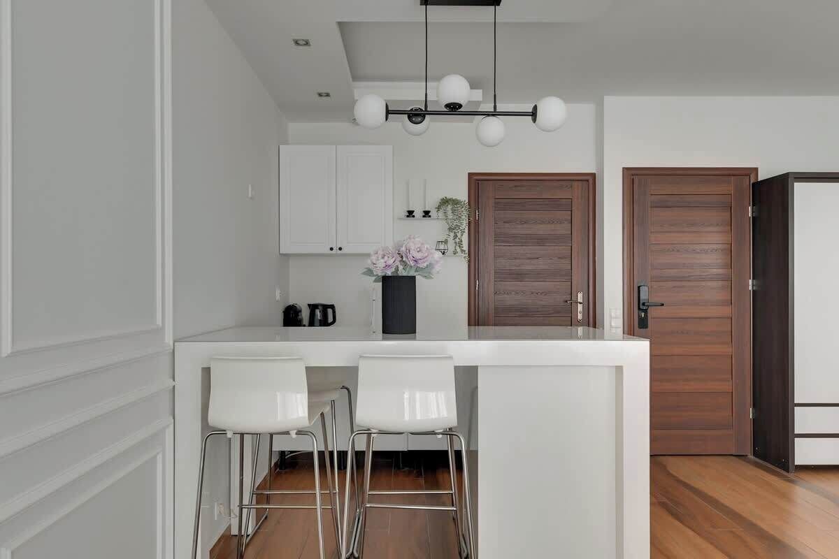 Eine moderne Küche mit weißen Schränken, einer Holztür und einer Bar mit weißen Hocker.