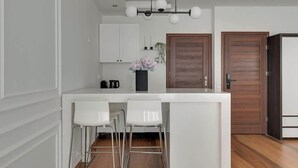 A modern kitchen with white cabinets, a wooden door, and a bar area with white stools. - Waterlane F9B | Spa, Pool & Gym | Riverside (Gdańsk)