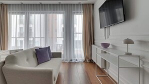 A modern living room with a sofa, a flat-screen TV mounted on the wall, a radiator, and a side table. - Waterlane F9B | Spa, Pool & Gym | Riverside (Gdańsk)