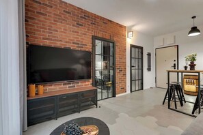 Ein modernes Wohnzimmer mit Backsteinwand, Flachbildfernseher, Essbereich mit Hockern und einer Bar.