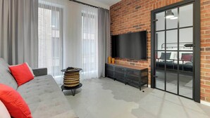 A modern living room with a grey sofa, a flat-screen TV, a brick wall, and a sliding glass door. - Granaria A212 | Best Location (Gdańsk)