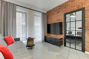 Ein modernes Wohnzimmer mit grauem Sofa, Flachbildfernseher, Backsteinwand und einer Schiebeglastür.