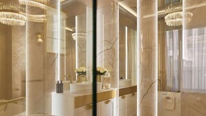 Ein luxuriöses Badezimmer mit großem Spiegel, Marmorsäulen, einer Badewanne und einem Schminktisch mit goldfarbenen Akzenten.