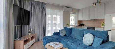 A modern living room with a blue sofa, a wooden coffee table, and a TV on a stand.