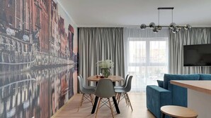 Un soggiorno moderno con zona pranzo, un'ampia finestra con tende, un televisore a schermo piatto montato a parete e un murale con vista sulla città.