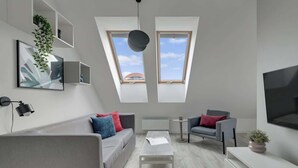 Una sala de estar moderna con un sofá gris, una mesa de centro, un televisor y dos tragaluces.