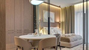 Ett modernt hotellrum med ett runt matbord, stolar, en soffa, en säng och ett stort fönster med gardiner.
