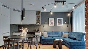 Un soggiorno moderno con un divano blu, un tavolo da pranzo con sedie e un angolo cucina con pensili e un piano di lavoro.