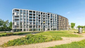 Un edificio moderno a più piani con balconi, una zona verde antistante e cielo sereno.