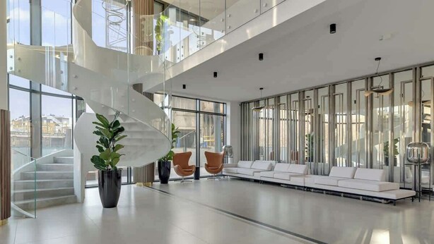 A modern interior with a spiral staircase, white sofas, and potted plants.