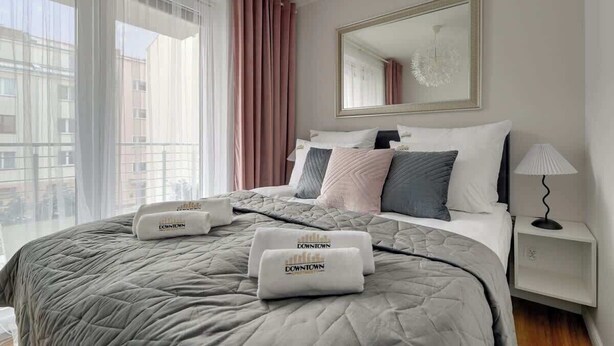 Ein Hotelzimmer mit einem großen Bett, einem Nachttisch, einem Spiegel und Blick auf Gebäude.