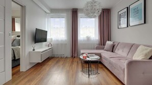 Ein modernes Wohnzimmer mit einer Couch, einem Fernseher, einem kleinen runden Tisch und einem Fenster mit Vorhängen.