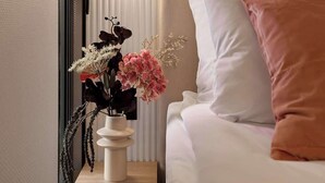 Ein Hotelzimmer mit einem Bett, einem Nachttisch mit Blumenvase und einer Wandleuchte.