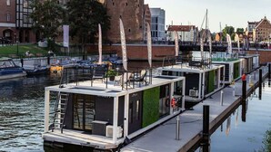 A floating houseboat docked at a pier with a cityscape in the background.