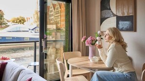 A room with a view of a canal, a table with a vase of flowers, and a modern abstract painting on the wall.