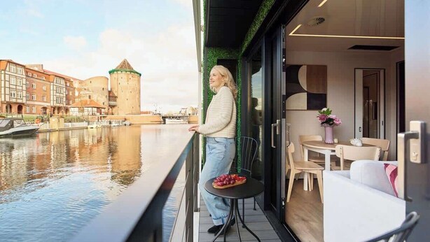Un balcone con vista su una torre storica, un'area pranzo con tavolo e sedie, e un interno moderno con un divano e un tavolino.
