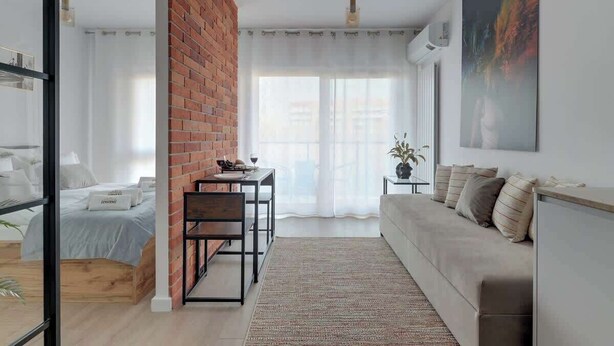 Een moderne woonkamer met een bakstenen muur, een bank, een eettafel en een bed.