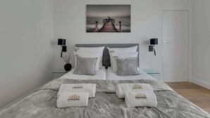 Une chambre à coucher bien rangée, avec un lit, des oreillers, un tableau accroché au mur, des lampes de chevet et une porte.
