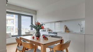 Une cuisine moderne avec des meubles blancs, une table à manger avec des chaises et une grande fenêtre donnant sur la ville.