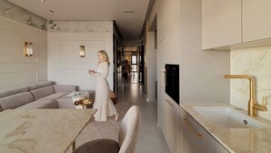 A modern kitchen with marble countertops, a gold faucet, and a dining area with a marble table and sofa. - Sol Marina Harmony | Perfect View (Gdańsk)