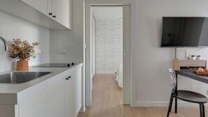 A modern kitchen with white cabinets, a stainless steel sink, and a flat-screen TV mounted on the wall. - Tartaczna 17 | Perfect Stay (Gdańsk)