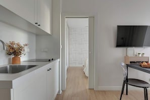 A modern kitchen with white cabinets, a stainless steel sink, and a flat-screen TV mounted on the wall. - Tartaczna 17 | Perfect Stay (Gdańsk)