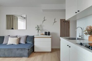 A modern kitchen with a built-in sink, a white countertop, and a wooden slatted wall. - Tartaczna 17 | Perfect Stay (Gdańsk)