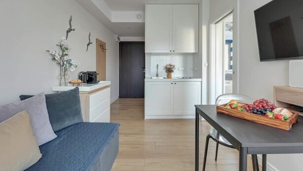 A modern living room with a sofa, a dining table with a fruit tray, a TV, and a kitchen in the background. - Tartaczna 17 | Perfect Stay (Gdańsk)