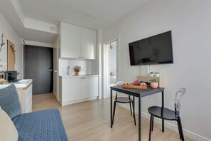 A modern kitchen with white cabinets, a dining area with a table and chairs, and a flat-screen TV mounted on the wall. - Tartaczna 17 | Perfect Stay (Gdańsk)