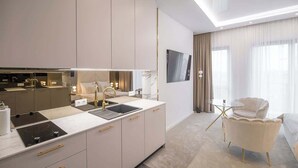 Ein modernes Hotelzimmer mit Küchenbereich, einem Flachbildfernseher, einem bequemen Sessel und einem Bett.