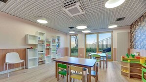 Een klaslokaal met een houten tafel, stoelen, planken en een uitzicht door de deur.