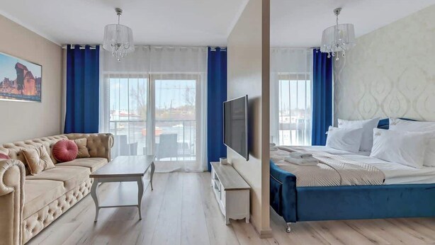 Een hotelkamer met een bank, een bed, een televisie en uitzicht op de stad.