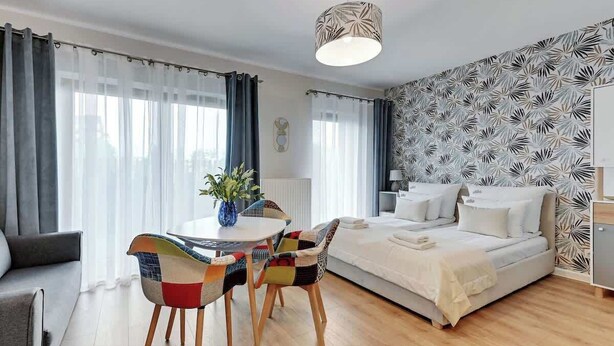 A modern hotel room with a bed, a dining table with chairs, a vase with flowers, and a patterned wall. - Nadmotławie 4 | Riverside | Sauna & Gym (Gdańsk)