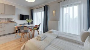 A modern hotel room with a bed, a dining area with chairs, a TV, and a large window with curtains. - Nadmotławie 4 | Riverside | Sauna & Gym (Gdańsk)