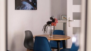 Un coin repas avec une table ronde en bois, des chaises bleues, un vase de fleurs et un tableau accroché au mur.