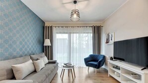 A living room with a sofa, a chair, a TV, a small table, and a ceiling fan. - Nadmotławie 5 | Riverside | Sauna & Gym (Gdańsk)