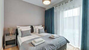A modern bedroom with a bed, nightstands, and a window with curtains. - Nadmotławie 5 | Riverside | Sauna & Gym (Gdańsk)