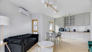 Een moderne woonkamer met een zwarte bank, een ronde marmeren salontafel en een eethoek met een kleine tafel en stoelen.