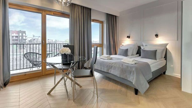 Ein modernes Hotelzimmer mit einem großen Bett, einem Esstisch mit Stühlen, einem Balkon mit Aussicht und einer Chandelüster.
