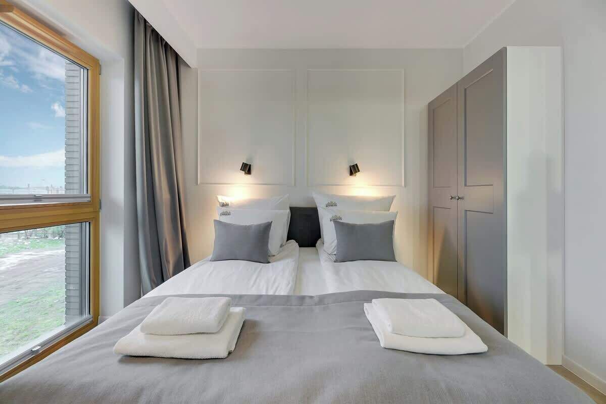 Quarto de hotel com uma cama grande, duas mesas de cabeceira, um guarda-roupa e uma janela com cortinas.