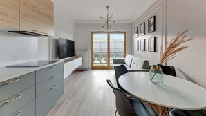 Moderni keittiö, jossa on televisio, puukaapit sekä ruokailutila pöytineen ja tuoleineen.