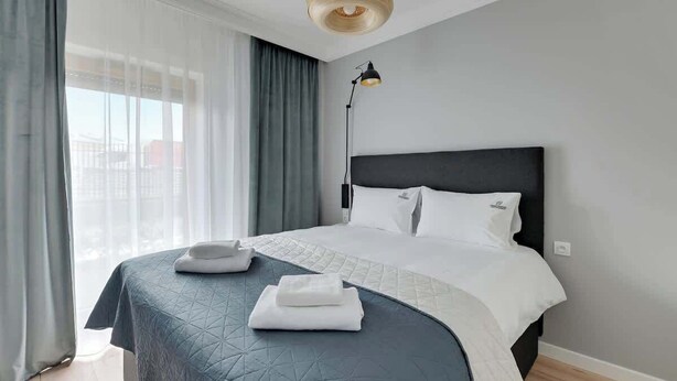 Hotellihuone, jossa on sänky, lamppu ja näkymä kaupunkiin.