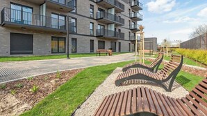 Een modern appartementencomplex met balkons, een geplaveid pad en buiten zitplaatsen.