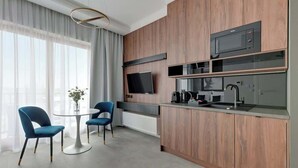 Een moderne keuken met een ingebouwde magnetron, een flatscreen televisie en een koffiezetapparaat. Er is een zithoek met twee stoelen en een tafel.
