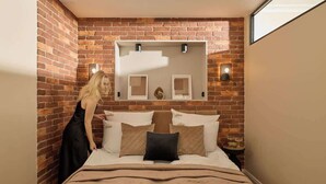 A hotel room with a brick wall, a bed with white and brown bedding, and a nightstand with a lamp. - Granaria B201 | Best Location (Gdańsk)