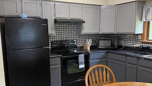 Una cucina con pensili grigi, un frigorifero nero, un piano cottura e un tavolo da pranzo con sedie.