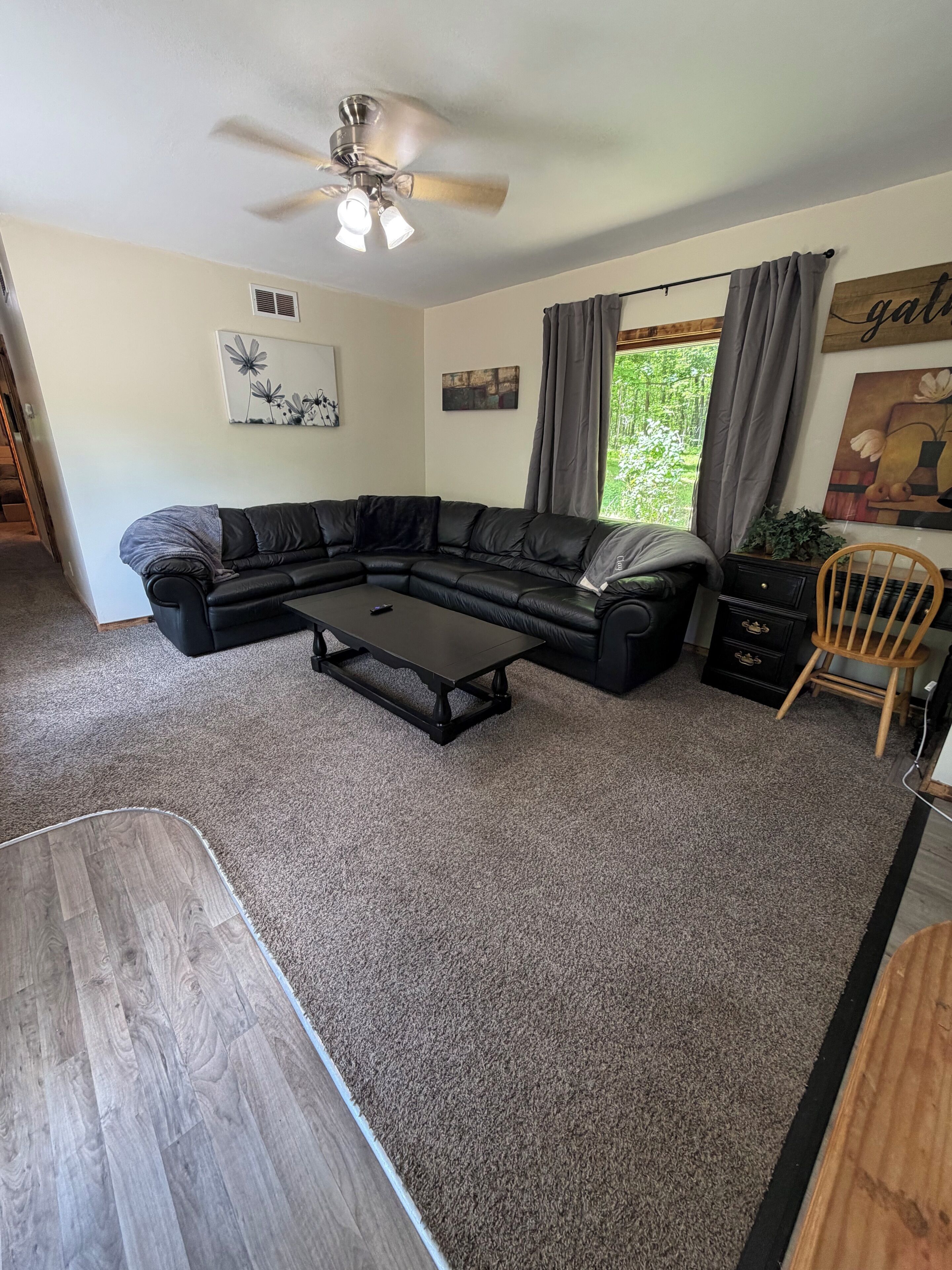 A living room with a sectional sofa, a coffee table, a ceiling fan, and artwork on the walls.